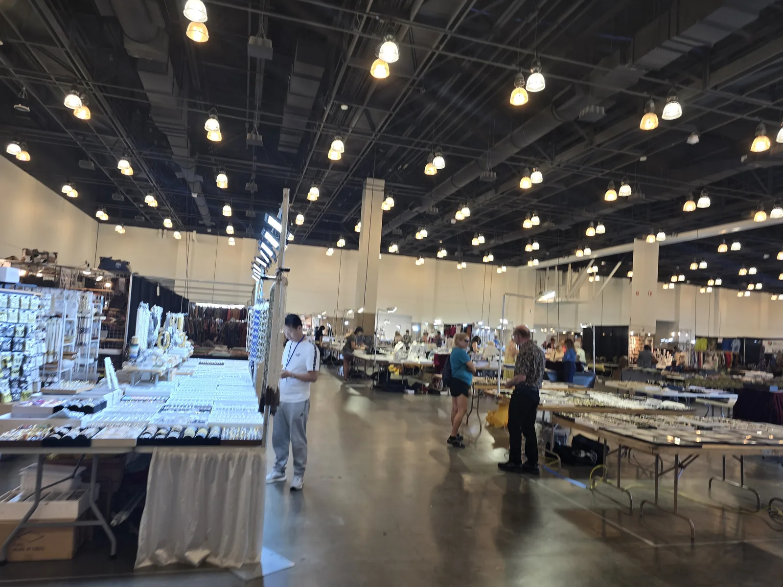 Pasadena 会议中心主展厅内景,高棚工业吊灯下成排折叠长桌铺满饰品,观众在过道间走动