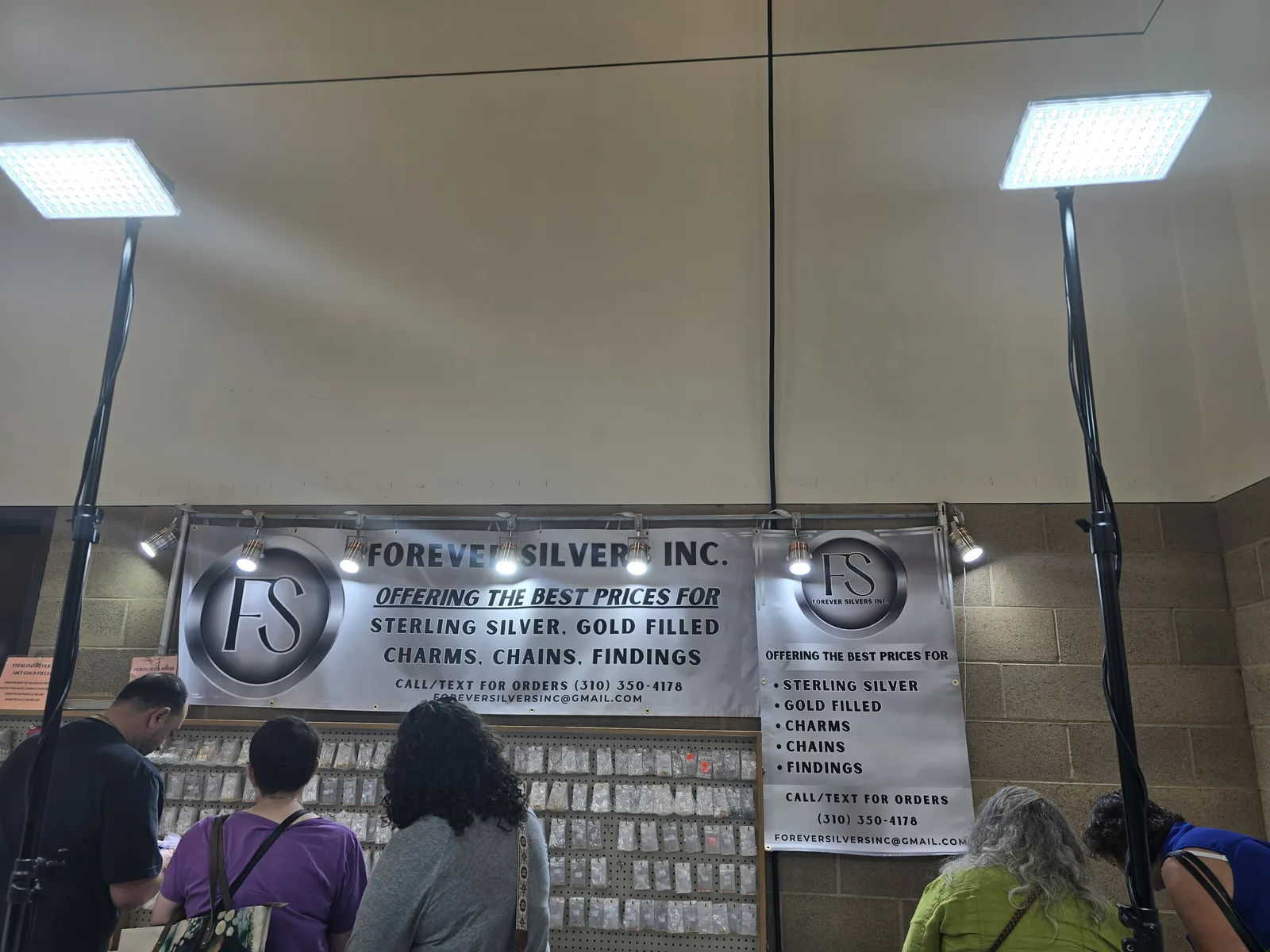 Forever Silver Inc 展位,横幅写着 OFFERING THE BEST PRICES FOR STERLING SILVER GOLD FILLED CHARMS CHAINS FINDINGS,下方整面洞洞板挂满小袋装配件,数名买家在挑选