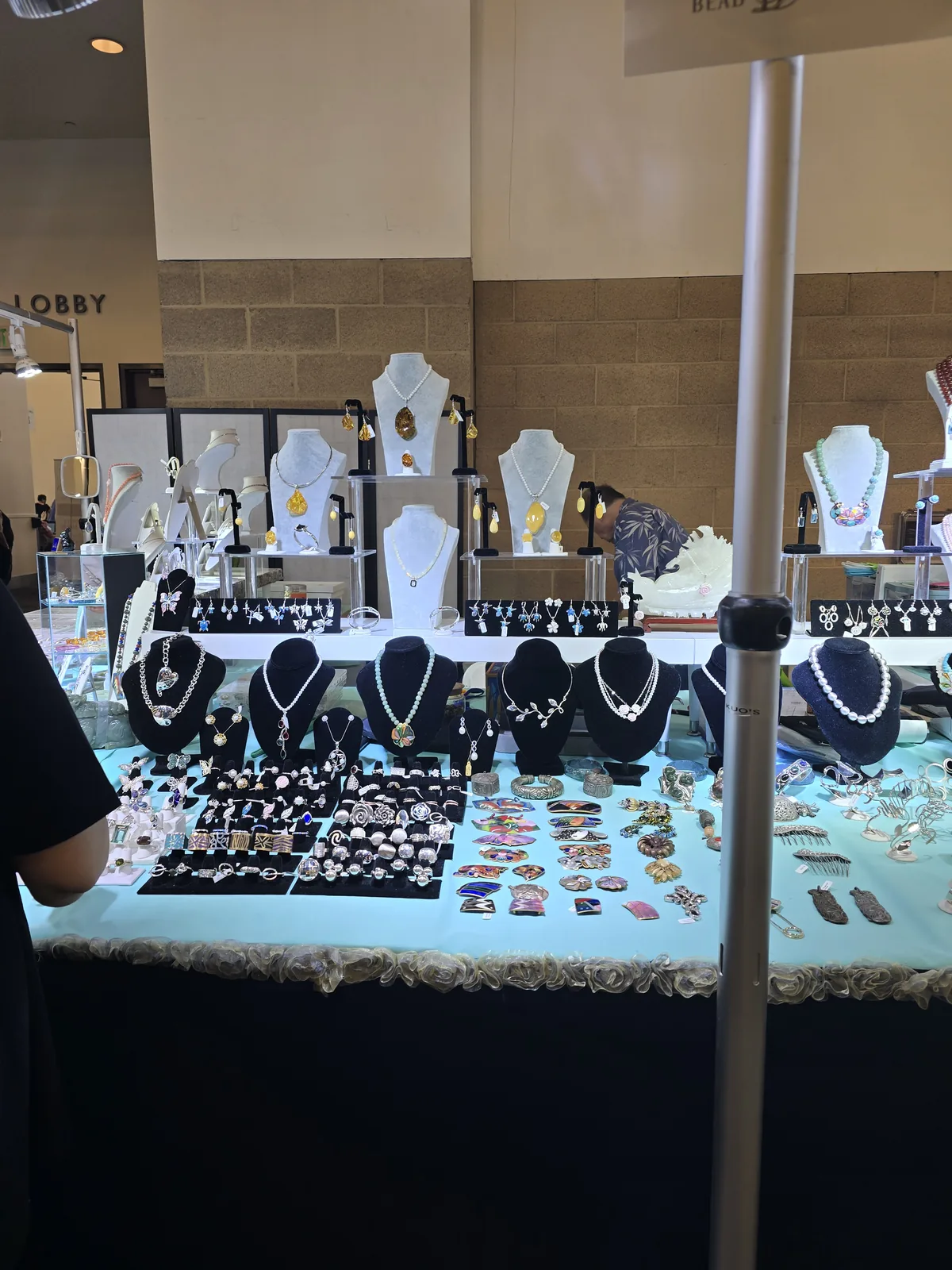 Kuo's Jewelry 展台近景,浅蓝台布上摆满银戒指板、景泰蓝胸针、珐琅发梳,后排展示琥珀吊坠与珍珠项链